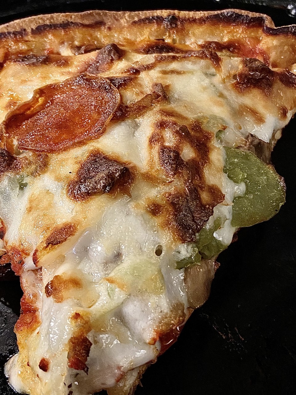 Close-up shot of a slice of pizza with melted cheese, pepperoni, and green bell pepper